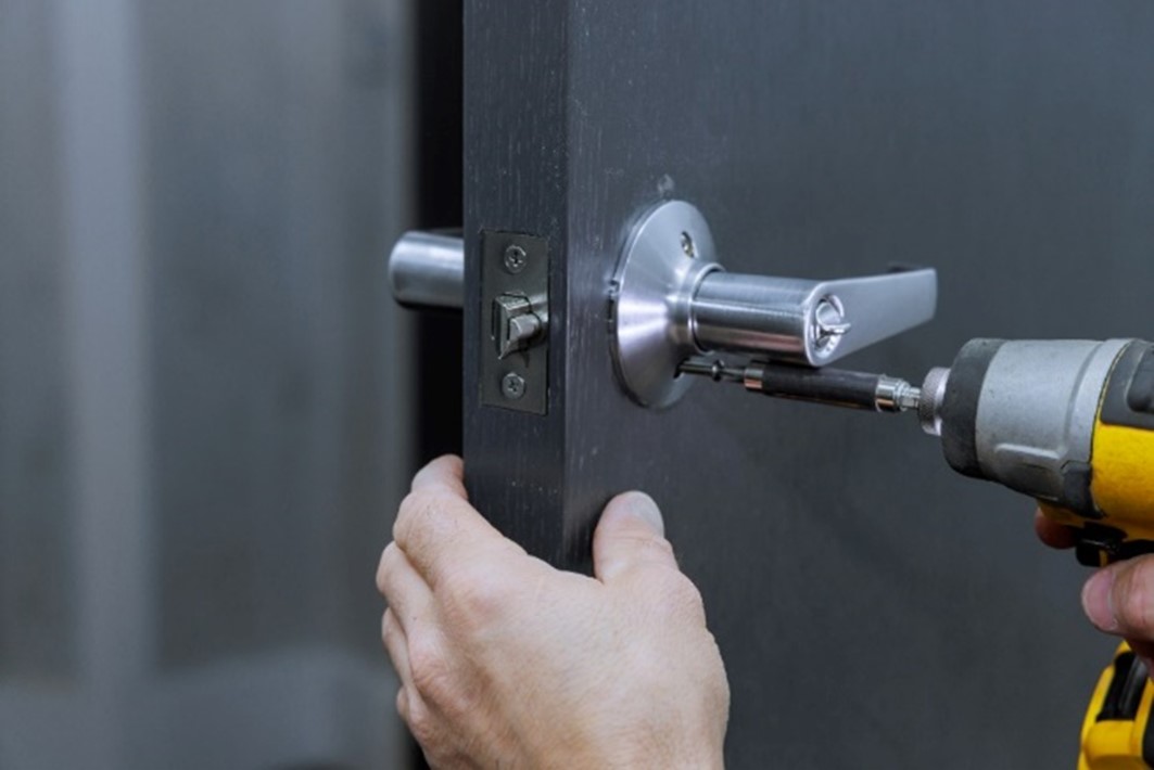 Close-up of a person using a power drill to fix an exterior door handle