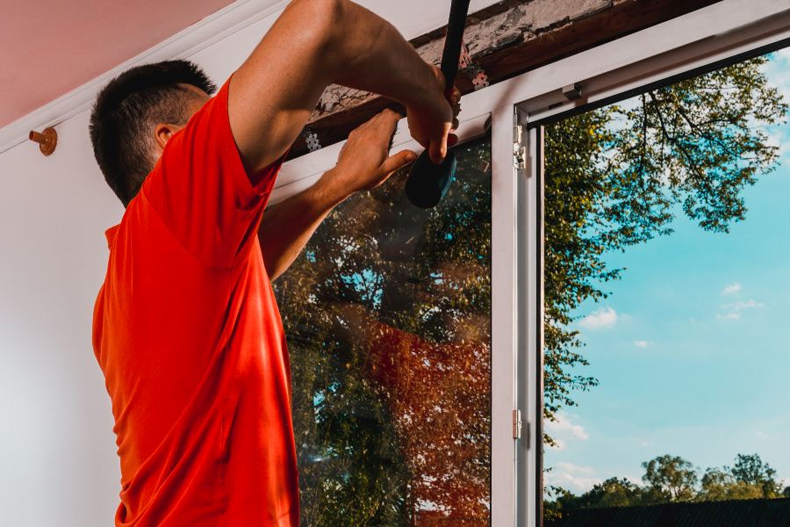 A person holding a hammer and using a window frame