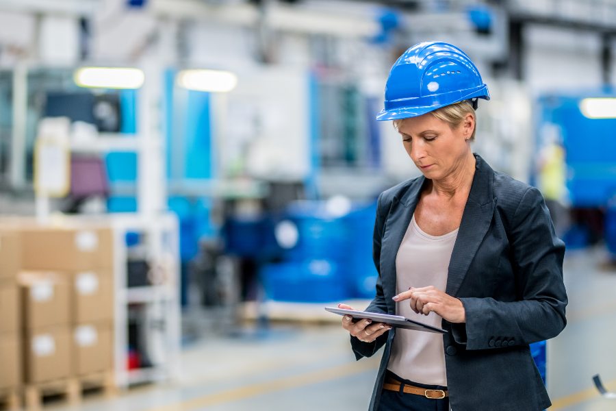 Factory manager wearing a safety helmet using a tablet on a manufacturing floor